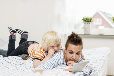 Mother and son using digital tablet lying in bed at home