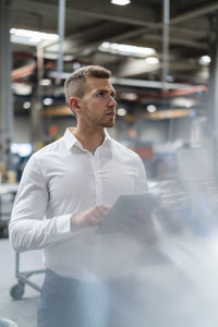 Young male inspector looking away while holding digital tablet in industry