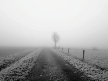 Road amidst trees on field against sky during winter