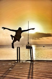 Silhouette man on jetty against sea at sunset