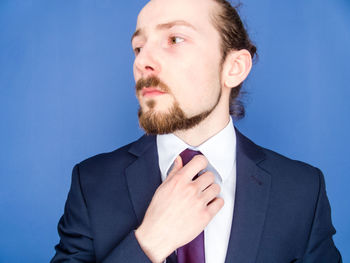 Young businessman adjusting tie against blue background