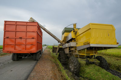 Yellow cart on road amidst field against sky