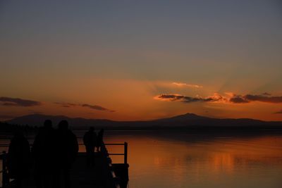 Silhouette people on pier over lake against sky during sunset