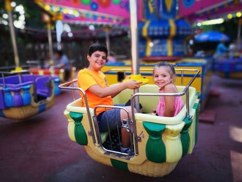 Tilt-shift image of happy siblings enjoying in amusement park ride