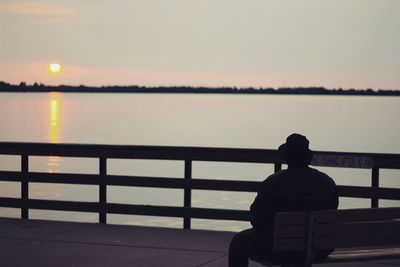 Rear view of man sitting on pier over sea against sky