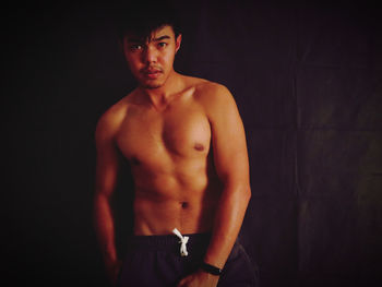 Portrait of young man standing against black background