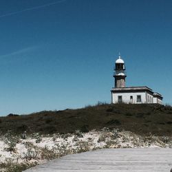 Lighthouse on beach against clear blue sky