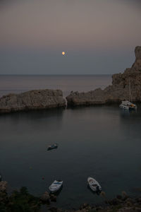 Scenicc view of coastline with calm water, boats and full moon at sunset. rhodes, dodecanese, greece