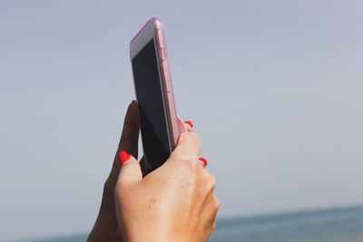 Close-up of hand holding smart phone against sky