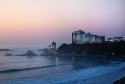 Buildings by sea against sky during sunset