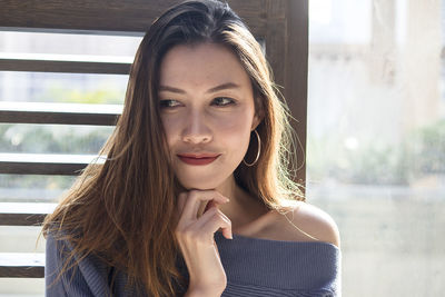 Close-up of thoughtful beautiful woman looking down while standing by window at home