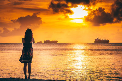 Silhouette woman standing on beach against sky during sunset