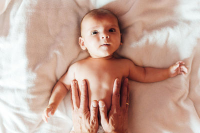 Top view of crop father touching peaceful infant lying on bed at home looking at camera