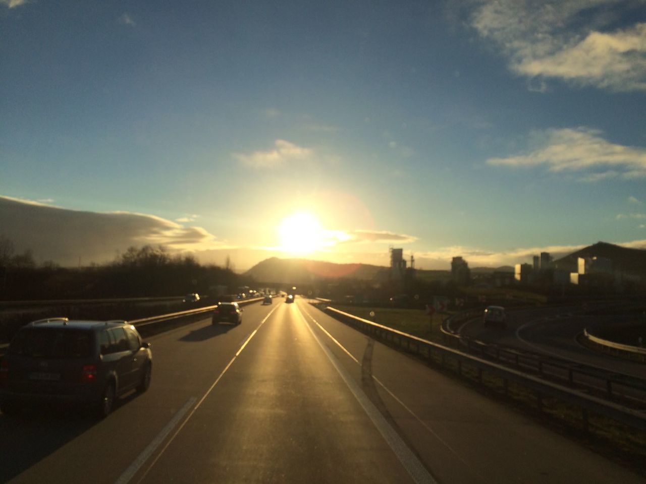 transportation, sunset, sun, car, road, land vehicle, the way forward, sky, mode of transport, sunlight, sunbeam, vanishing point, diminishing perspective, lens flare, street, built structure, cloud - sky, road marking, architecture, building exterior