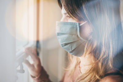 Woman looking outside the window with surgical mask during coronavirus lockdown. covid-19 people