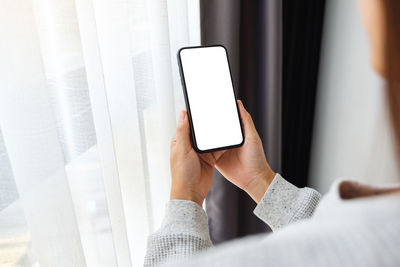 Mockup image of a woman holding mobile phone with blank white desktop screen