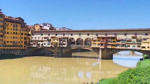 Arch bridge over river in city against clear sky