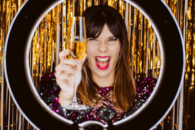 Portrait of laughing young woman holding champagne flute against colored background