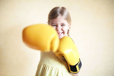 Portrait of smiling girl wearing boxing gloves against beige background