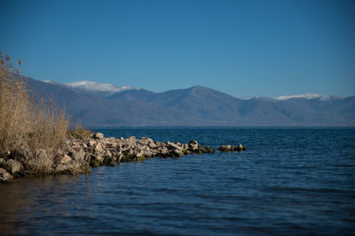 Scenic view of lake and mountains against clear blue sky