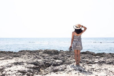 Rear view of young woman standing at beach against clear sky