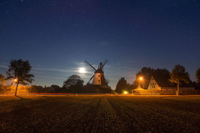 Illuminated traditional windmill on field against sky at night