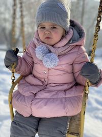 Cute girl sitting on swing during winter