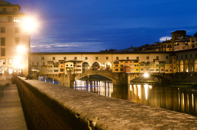 Illuminated ponte vecchio over arno river against sky at night