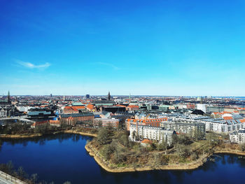 Buildings by river against clear blue sky