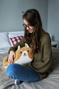 Millennial brown-haired girl in cat ears sits on a bed with a toy