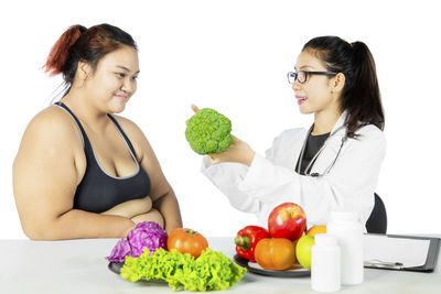 Dietitian showing vegetable to overweight patient against white background