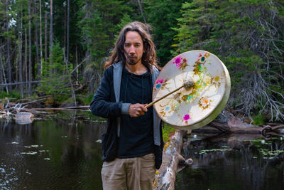 Portrait of man standing by lake in forest