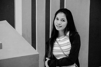 Portrait of young woman smiling while standing against wall