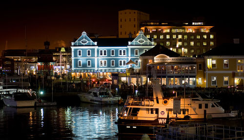 Boats moored at harbor against illuminated buildings at night