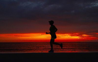 Silhouette man standing on beach against sky during sunset