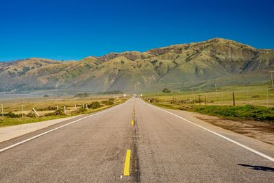 Road leading towards mountains against blue sky