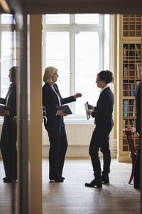 Senior lawyer discussing with female coworker while standing in library seen from doorway