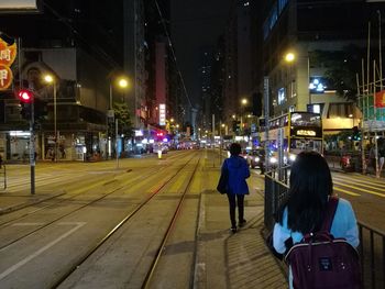 Rear view of people walking on illuminated street at night