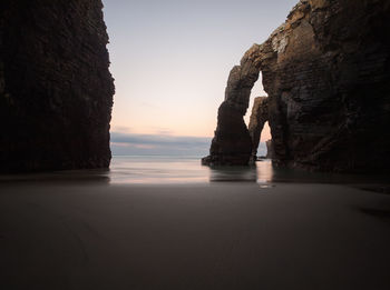 Rock formation on beach against sky during sunset