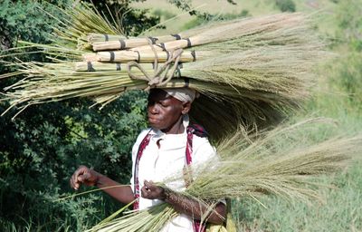 High angle view of senior woman carrying brooms on head while walking amidst plants
