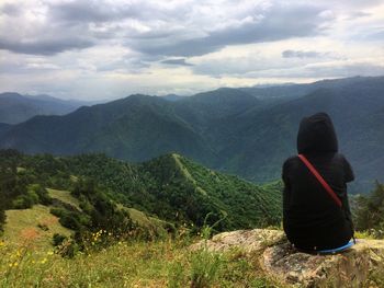 Rear view of woman sitting on mountain against sky