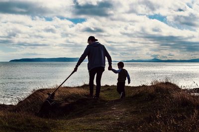 Full length of friends standing on sea shore against sky