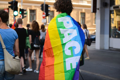 Rear view of man wearing rainbow flag during parade in city