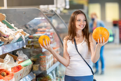 Smiling woman holding pumpkin standing at store