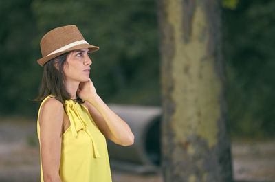 Young woman wearing hat standing against tree