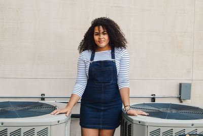 Portrait of young woman with curly hair standing against wall