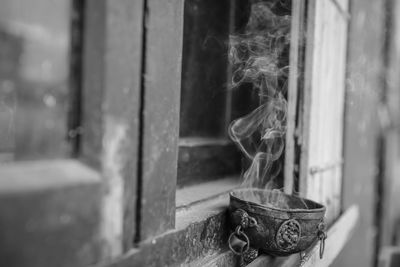 Close-up of smoke emitting from bowl on window sill