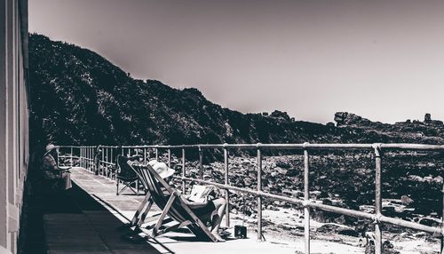 Person sitting on deck chair by railing against clear sky