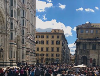 People on street amidst buildings in city against sky