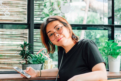 Portrait of young woman with mobile phone sitting in cafe